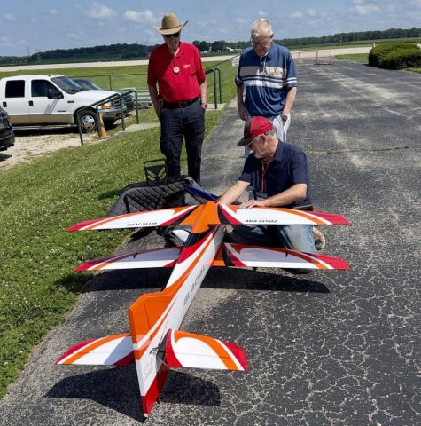 Model airplane on a runway with three men nearby, one kneeling to inspect it.
