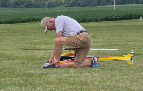Man kneeling on grass beside a model helicopter, adjusting its components.