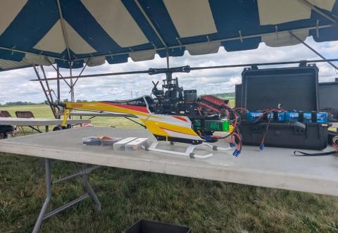 RC helicopter on a table under a canopy, grassy field in the background.