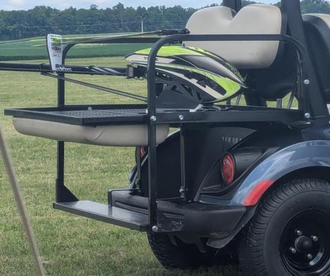 Golf cart with a green helmet on a rear rack, parked on grass.