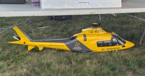 Yellow and black model helicopter on grass under a table.