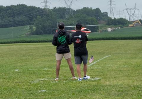 Two people flying a model helicopter in a grassy field.