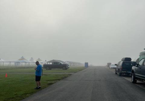 Foggy road with cars, tents, and a person in blue using a phone.