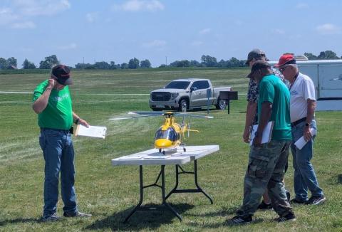 Model plane on a table outdoors, surrounded by five people inspecting it.