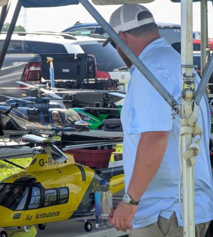Remote-controlled helicopters on display at an outdoor event, with a man observing.