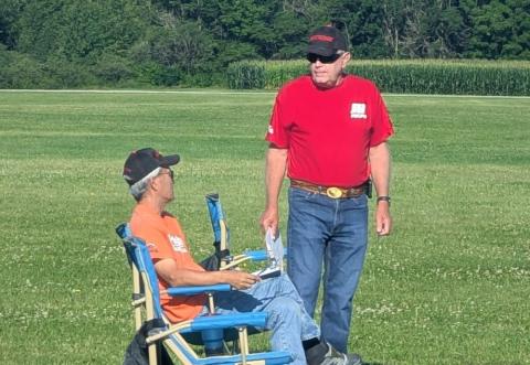 Two men in casual clothes talking in a grassy field.