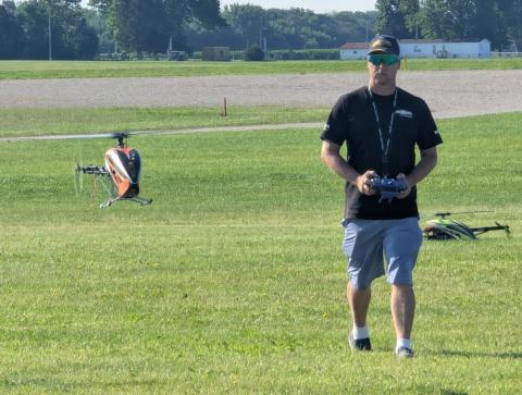 Man controlling a model helicopter in a grassy field.