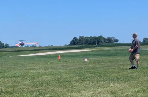 Remote control helicopter flying in an open grassy field.