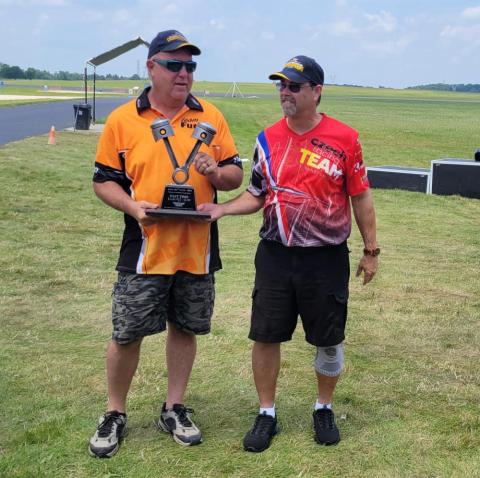 Two men in sports shirts holding a trophy on a grassy field.