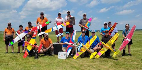 Group holding colorful model airplanes on a grassy field.