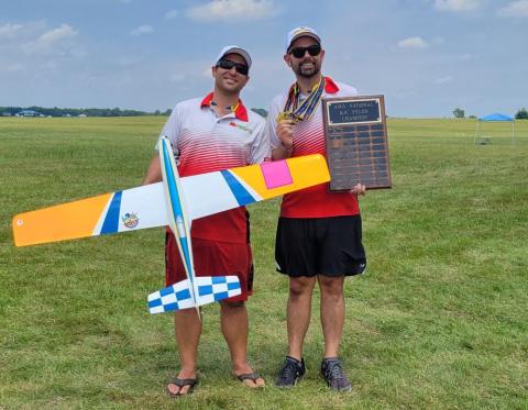 Two men in matching uniforms, one holding a model plane, the other a plaque.