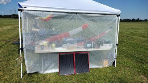 A canopy with equipment and a large model plane on a grassy field.