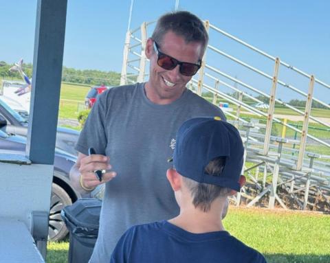 A man in sunglasses signs an autograph for a young boy outdoors.