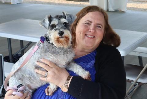 Smiling woman holding a small gray dog on her lap.