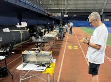 Indoor track event, man writes on paper near tables with equipment and flags.