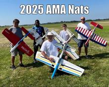 Five people holding model airplanes on a grassy field.