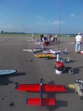 Toy airplanes lined up on a runway, people preparing them for flight.