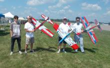 Four people holding large colorful model airplanes outdoors.