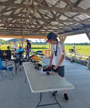 Man working with equipment at a picnic shelter, open field in background.