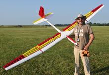 Man holding large model glider on grass field, wearing a sun hat and sunglasses.