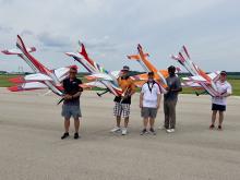 Five people holding colorful model airplanes on an airfield runway.