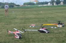 Remote-controlled helicopters on grass, with operator nearby.